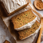 Sliced pumpkin zucchini bread with cream cheese frosting on parchment paper, topped with cinnamon and surrounded by warm fall spices.