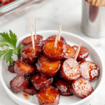 BBQ sausage bites served on a white plate with toothpicks, glazed in sticky barbecue sauce.