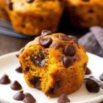 Moist pumpkin chocolate chip muffin with melty chocolate on a white plate, perfect for fall baking.