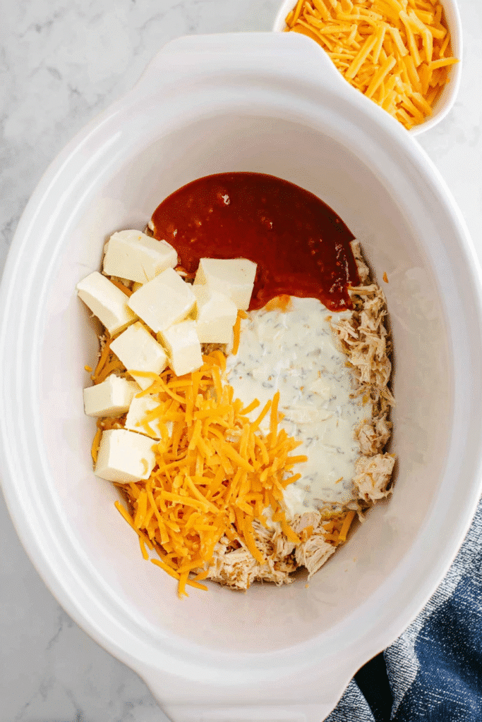 Crock Pot filled with shredded chicken, cheddar cheese, ranch dressing, cream cheese, and buffalo sauce for Buffalo Chicken Dip.