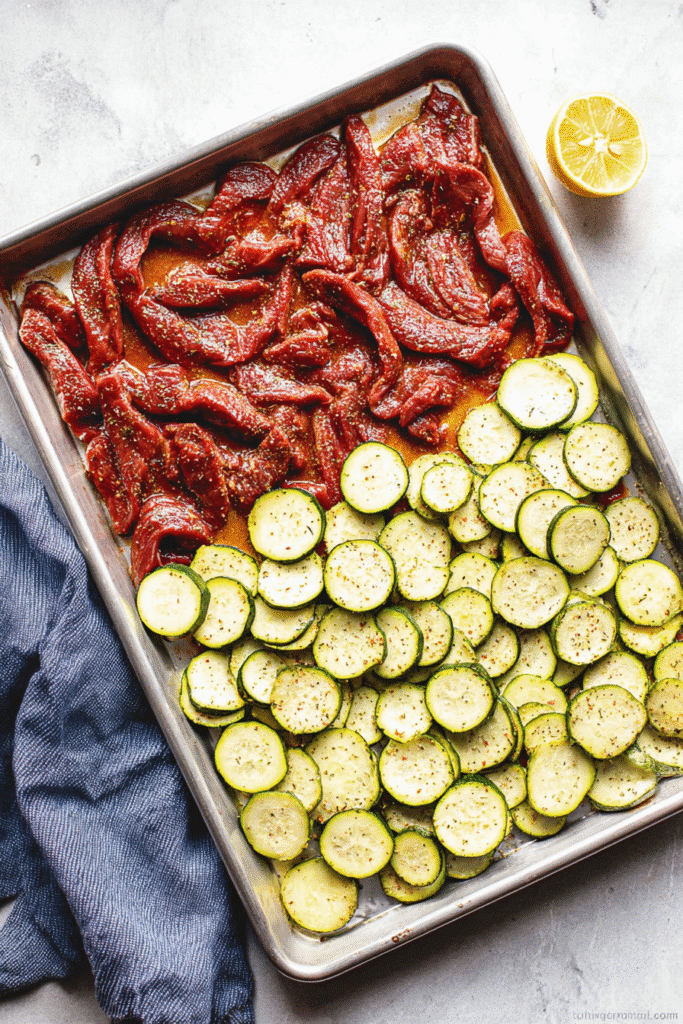 Sheet pan with raw marinated steak and zucchini ready for sheet pan steak with lemon zucchini.