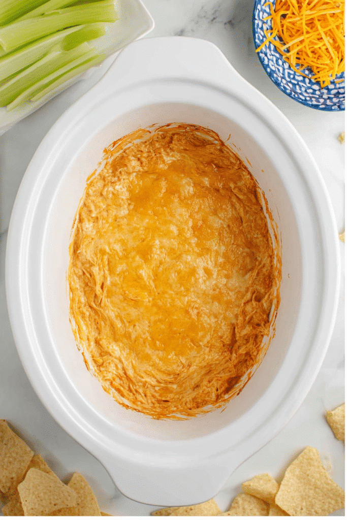 Fully cooked Buffalo Chicken Dip in a Crock Pot with golden melted cheese on top