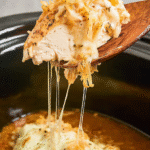 Melted cheese-topped Crock Pot French Onion Chicken being lifted from the slow cooker with a wooden spoon, showing gooey cheese pull.