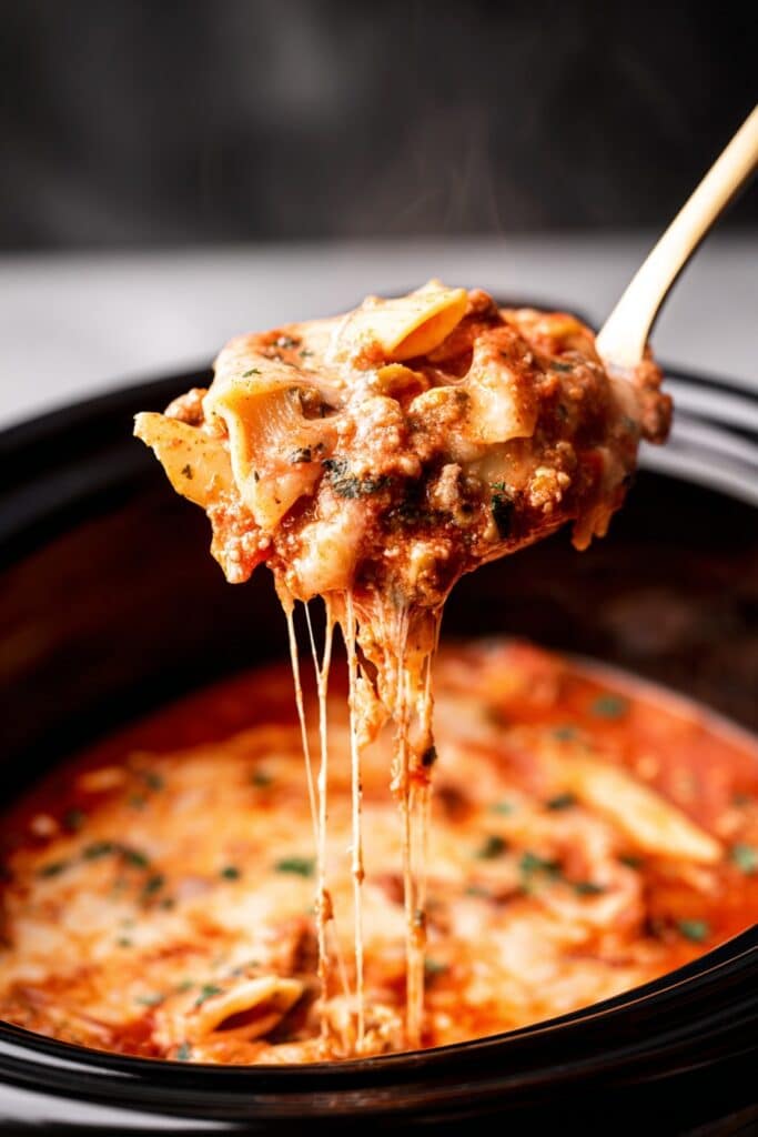 Ladle lifting cheesy slow cooker lasagna soup with rich tomato sauce, noodles, and herbs from a black crockpot.