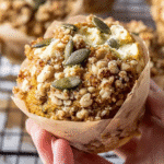 Hand holding a gluten free pumpkin cream cheese muffin with streusel topping and visible cream cheese center.