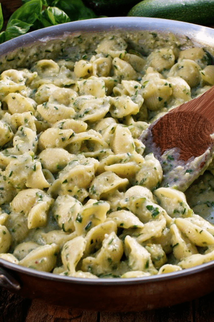 Creamy zucchini pasta with shells in skillet, stirred with wooden spoon