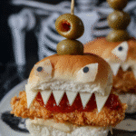 Spooky Halloween Chicken Parmesan Sliders with cheese teeth and olive eyes on a skeleton-themed plate.