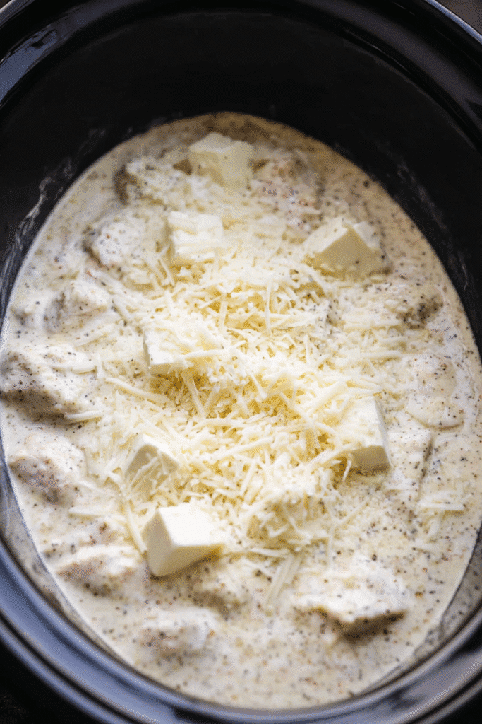 Crockpot filled with garlic parmesan sauce, cream cheese, and shredded parmesan over chicken for Crockpot Garlic Parmesan Chicken Pasta.
