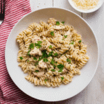 Creamy Crockpot garlic parmesan chicken pasta topped with parsley in a white bowl on rustic wooden table.