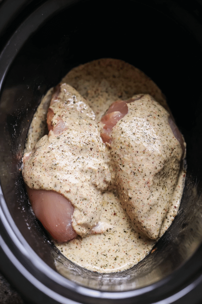 Raw chicken breasts in a crockpot covered with creamy garlic parmesan sauce for Crockpot Garlic Parmesan Chicken Pasta.