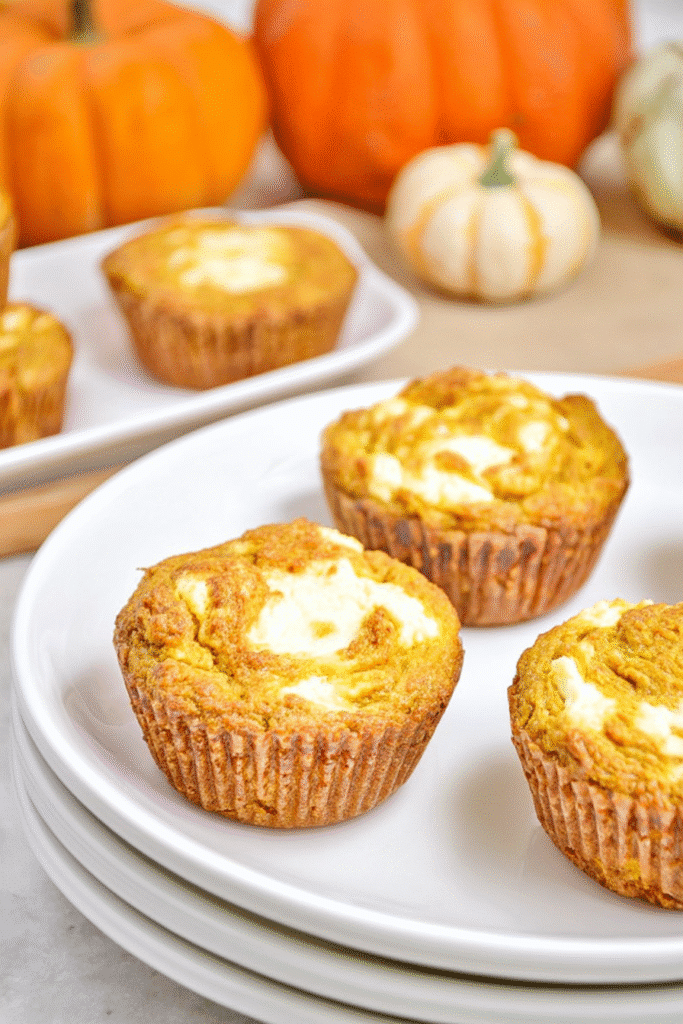 Keto pumpkin cream cheese muffins with swirled tops on a white plate, perfect for fall baking.