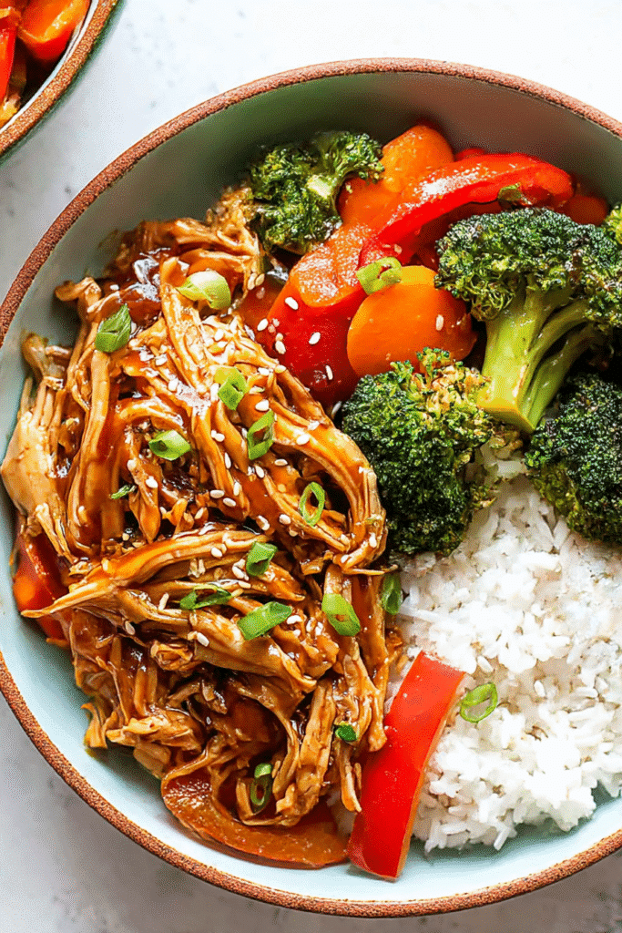 Overhead bowl of easy crock pot teriyaki chicken with rice, broccoli, peppers, carrots, and sesame seeds.
