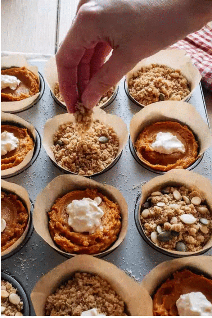 Topping gluten free pumpkin cream cheese muffin batter with crumb streusel and pumpkin seeds before baking.