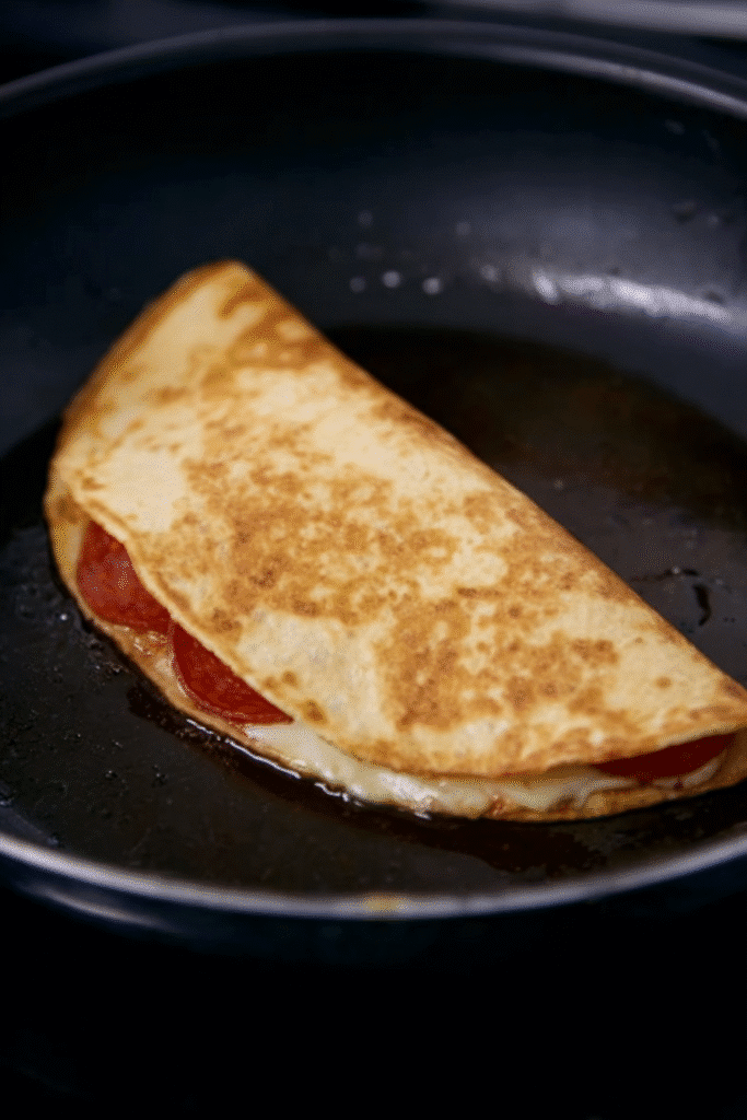 Crispy folded pepperoni pizzadilla browning in a skillet with melted cheese peeking out.