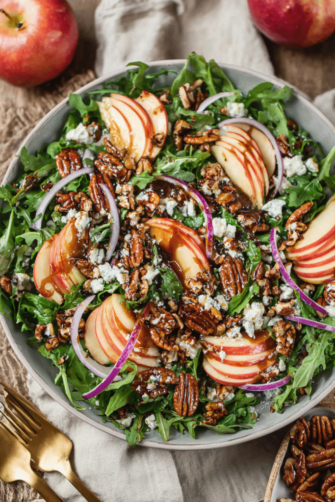 Fresh apple arugula salad with pecans, feta, red onions, and balsamic drizzle in a rustic ceramic bowl.