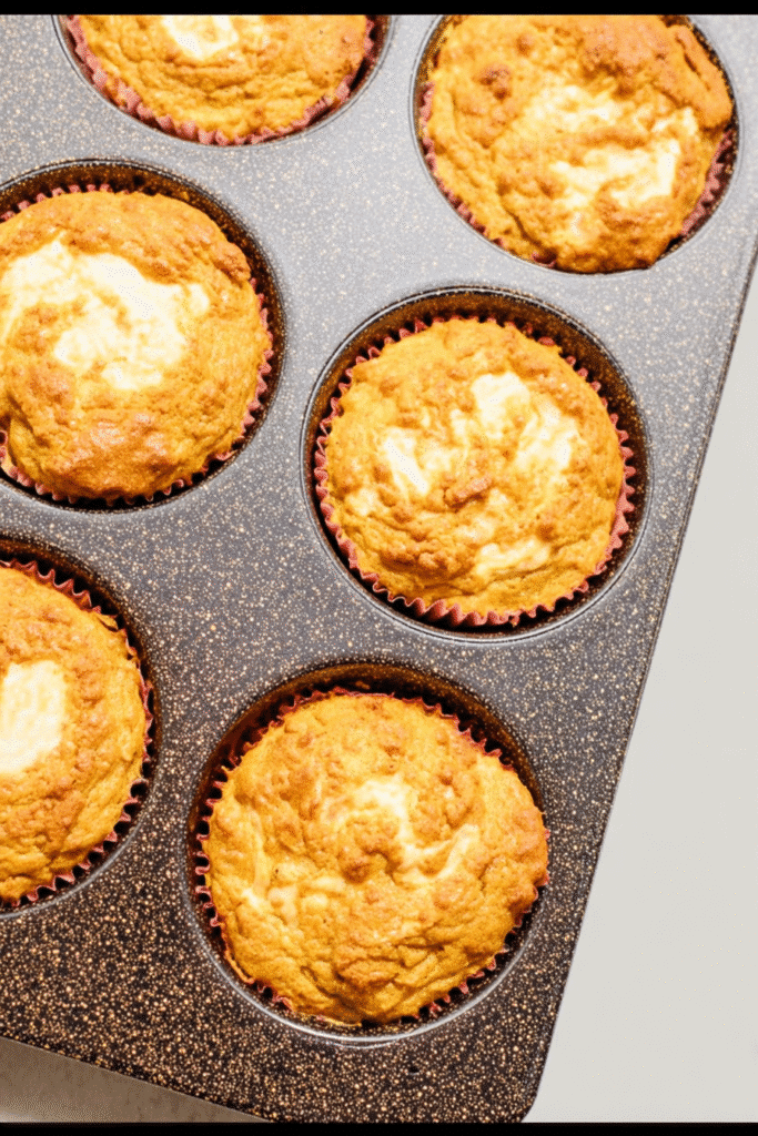 Overhead view of keto pumpkin cream cheese muffins in a speckled muffin tin, showing creamy swirled tops.