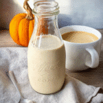 Glass bottle of pumpkin spice coffee creamer with pumpkin and coffee on linen