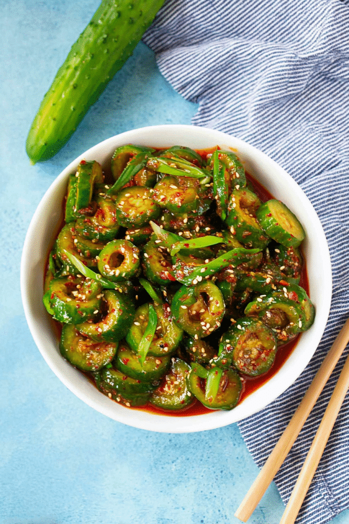 Finished Korean cucumber salad with spiral-cut cucumbers in red chili dressing, topped with sesame seeds and garlic.