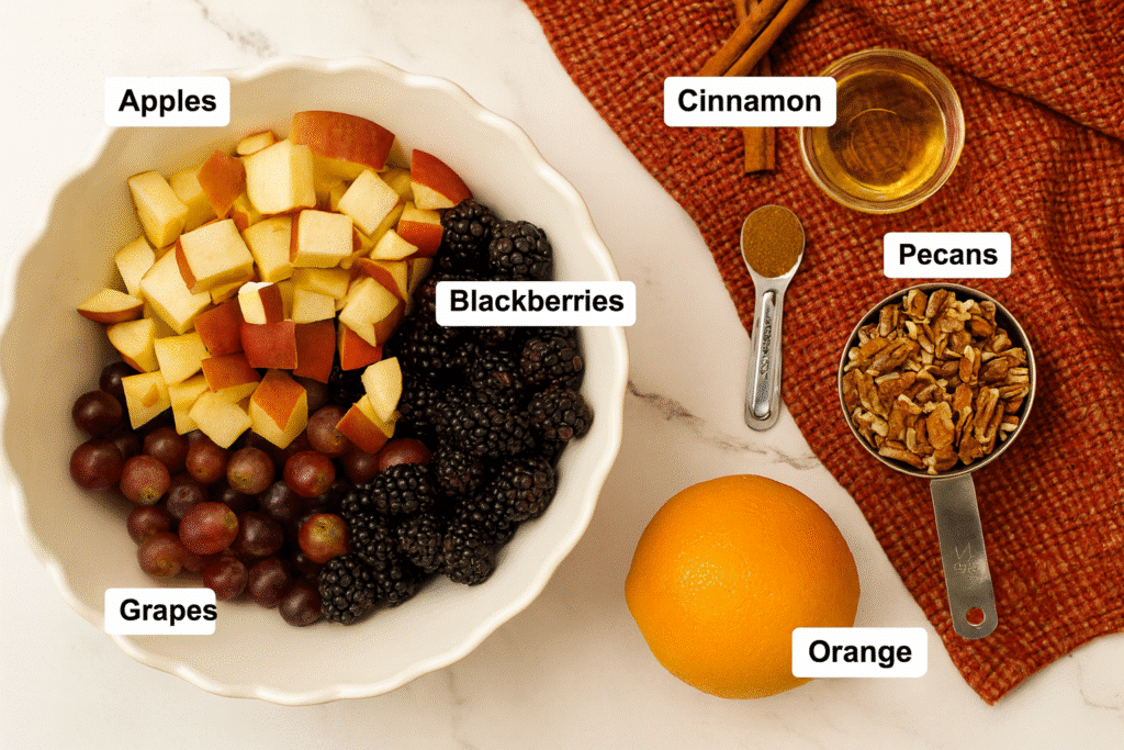 Flat lay of fall fruit salad ingredients with apples, grapes, blackberries, pecans, cinnamon, and orange