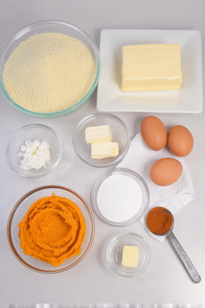 Flat lay of keto pumpkin cream cheese muffin ingredients including creamy pumpkin puree, almond flour, cream cheese, eggs, and butter.