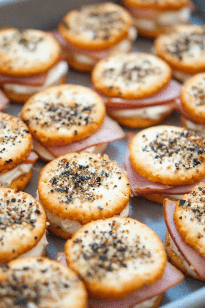 Ritz Cracker Party Sandwiches stacked on a tray with ham, cream cheese, and cracked black pepper topping.