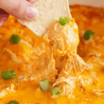 Tortilla chip scooping creamy, cheesy Buffalo Chicken Dip in a Crock Pot topped with green onions.