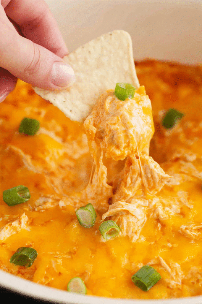 Tortilla chip scooping creamy, cheesy Buffalo Chicken Dip in a Crock Pot topped with green onions.