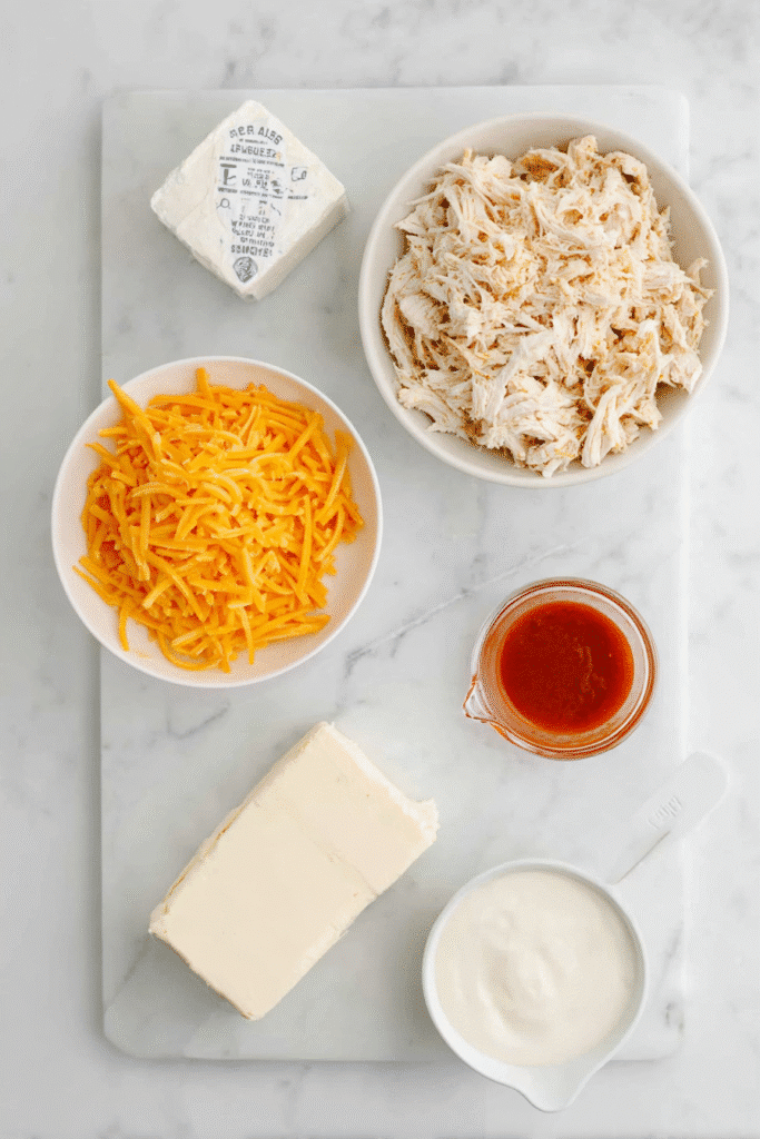 Ingredients for Buffalo Chicken Dip in a Crock Pot including shredded chicken, cheddar cheese, ranch dressing, hot sauce, and cream cheese.