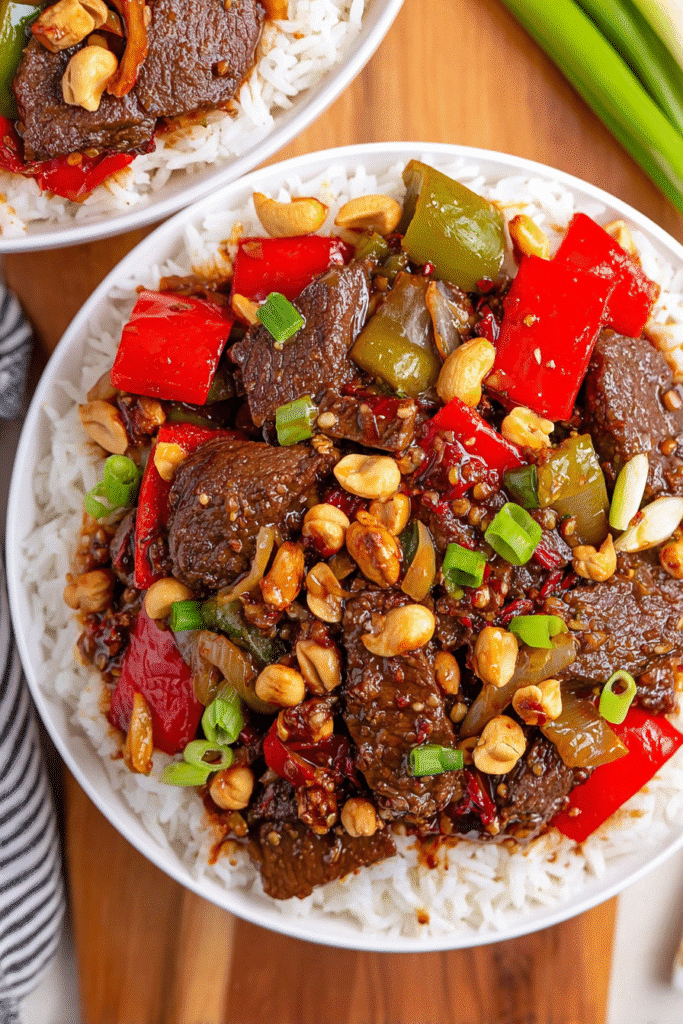 Kung Pao Beef with bell peppers, peanuts, and rice in a white bowl