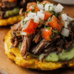 Close-up of Mexican tostada topped with carne asada, avocado crema, and pico de gallo
