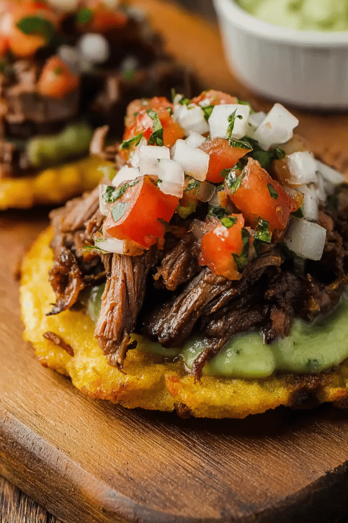 Close-up of Mexican tostada topped with carne asada, avocado crema, and pico de gallo