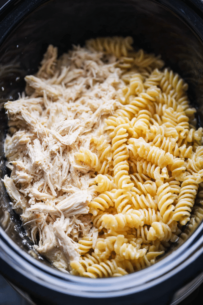 Mixing Crockpot Garlic Parmesan Chicken Pasta with creamy sauce and shredded chicken