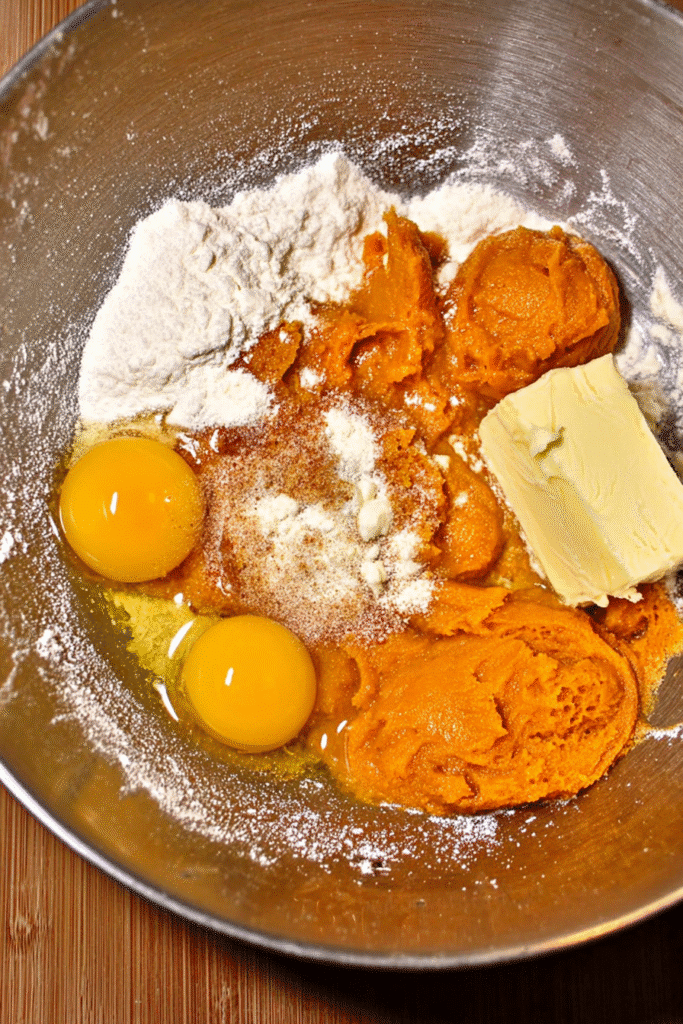 Keto pumpkin cream cheese muffin ingredients including eggs, butter, pumpkin puree, and spices in a mixing bowl.
