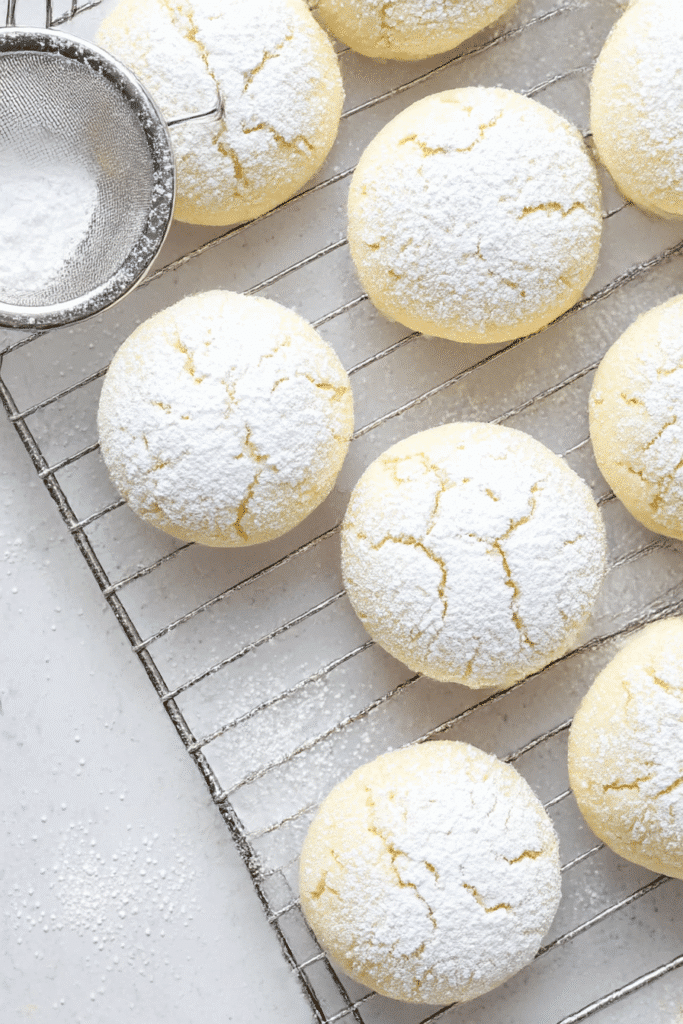 Cream cheese cookies being dusted with powdered sugar in a close-up baking shot.