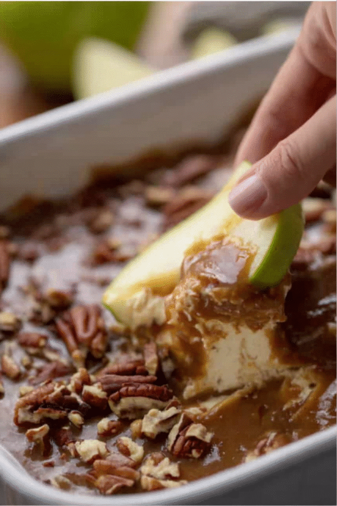 Dipping a green apple slice into an easy caramel apple cheesecake dip with pecans.