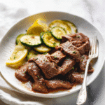 Plated sheet pan steak with lemon zucchini served with lemon slices.