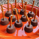 Mini chocolate Witch’s Broomsticks made from peanut butter cups and pretzels on an orange plate.
