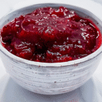 Homemade red berry jam in a rustic white bowl on a marble surface