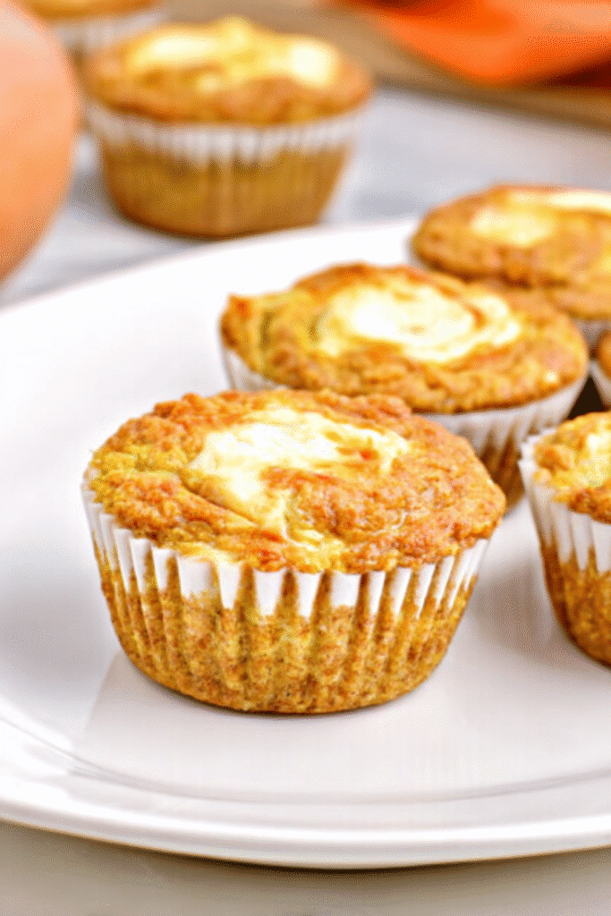Close-up of a keto pumpkin cream cheese muffin with a creamy swirl top on a white plate.