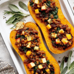 Apple Sausage Stuffed Butternut Squash with apples, sausage, cranberries, spinach, and pecans on a white baking tray