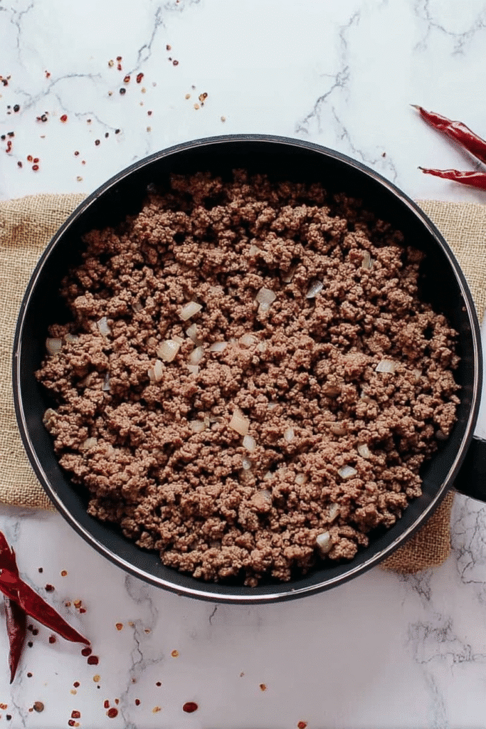 Browning ground beef with onions in a skillet for easy crockpot chili.