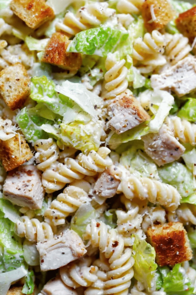 Close-up of Chicken Caesar Pasta Salad with creamy rotini, lettuce, grilled chicken, croutons, and parmesan.

