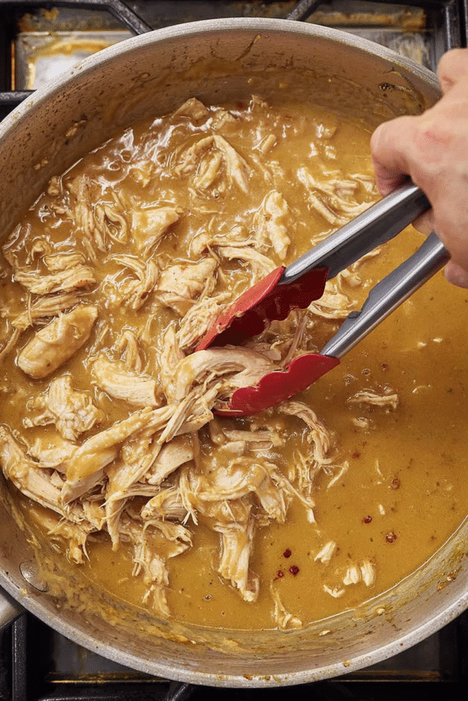 Shredded chicken mixed into golden gravy in a skillet for homestyle chicken and gravy.