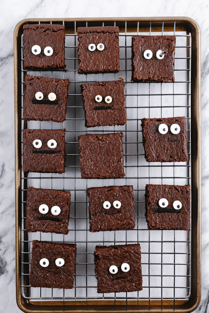 Chocolate brownies cooling on a rack, some with candy eyes for mummy brownies.