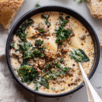 Hearty creamy white lasagna soup with sausage, kale, and lasagna noodles in a black bowl, served with rustic bread.
