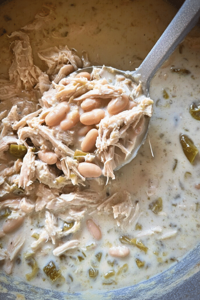 Ladle of creamy white chicken chili with shredded chicken, white beans, and green chiles in a thick, creamy broth.