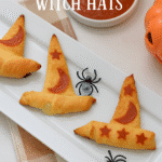 Golden crescent roll witch hats decorated with pepperoni moon and stars, served on a white platter with marinara sauce and Halloween decorations.