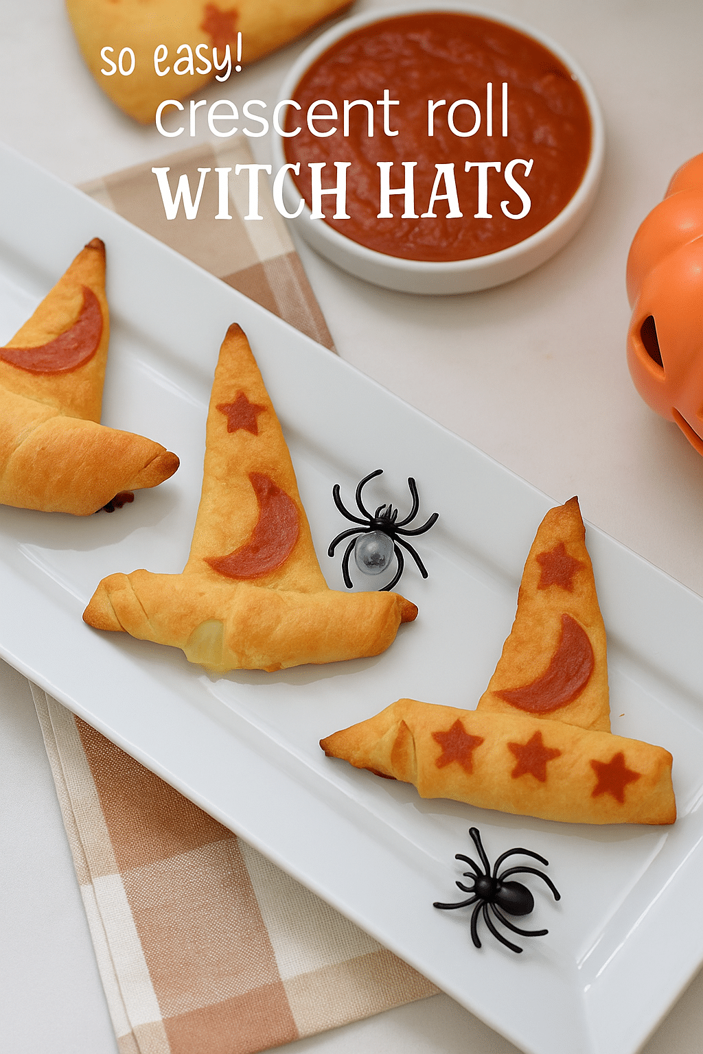 Golden crescent roll witch hats decorated with pepperoni moon and stars, served on a white platter with marinara sauce and Halloween decorations.