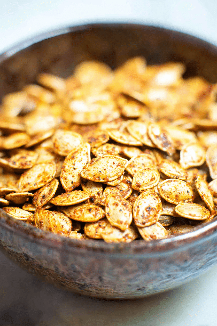 Golden-brown roasted pumpkin seeds in a rustic ceramic bowl, seasoned with spices for a crunchy autumn snack.