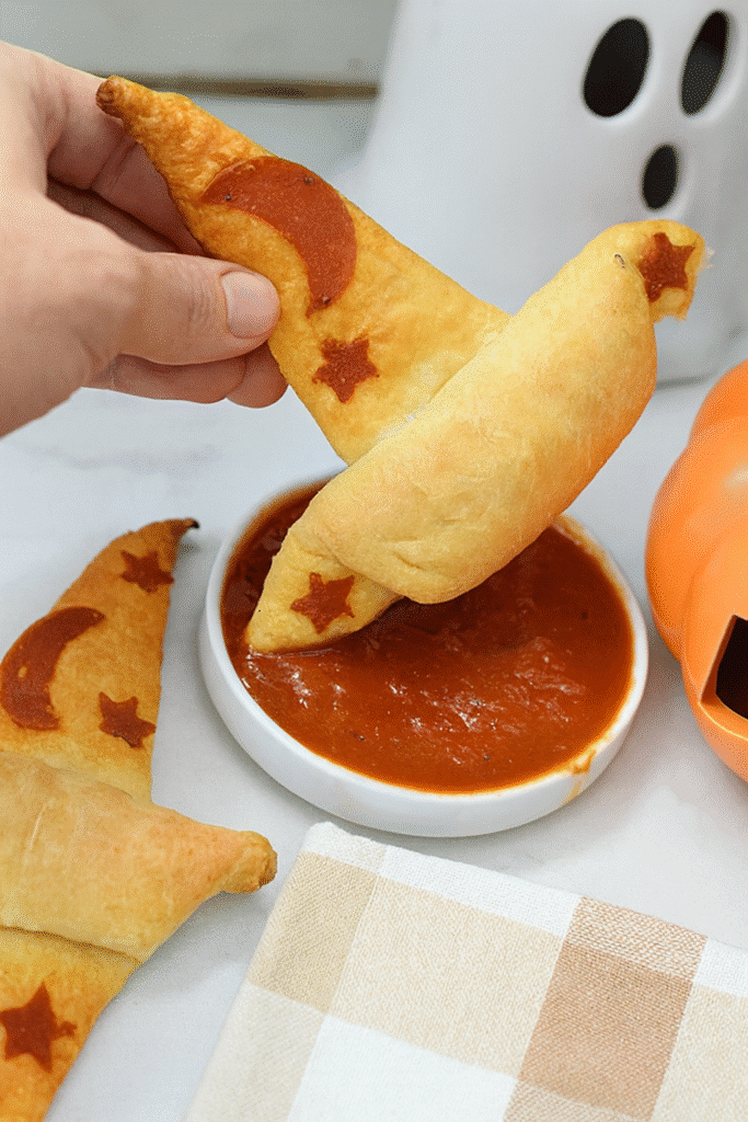Halloween-themed Crescent Roll Witch Hats with pepperoni moon and star decorations, served with marinara dipping sauce.